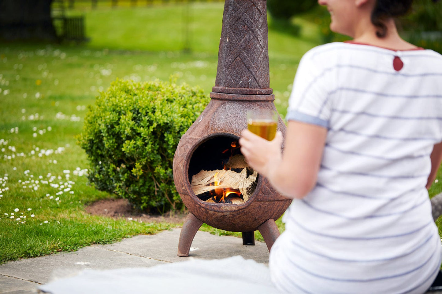 Person sitting by a chiminea in a garden holding a drink