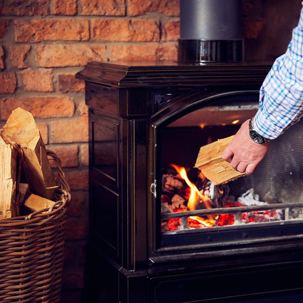 Person loading wood into a lit wood stove against a brick wall.