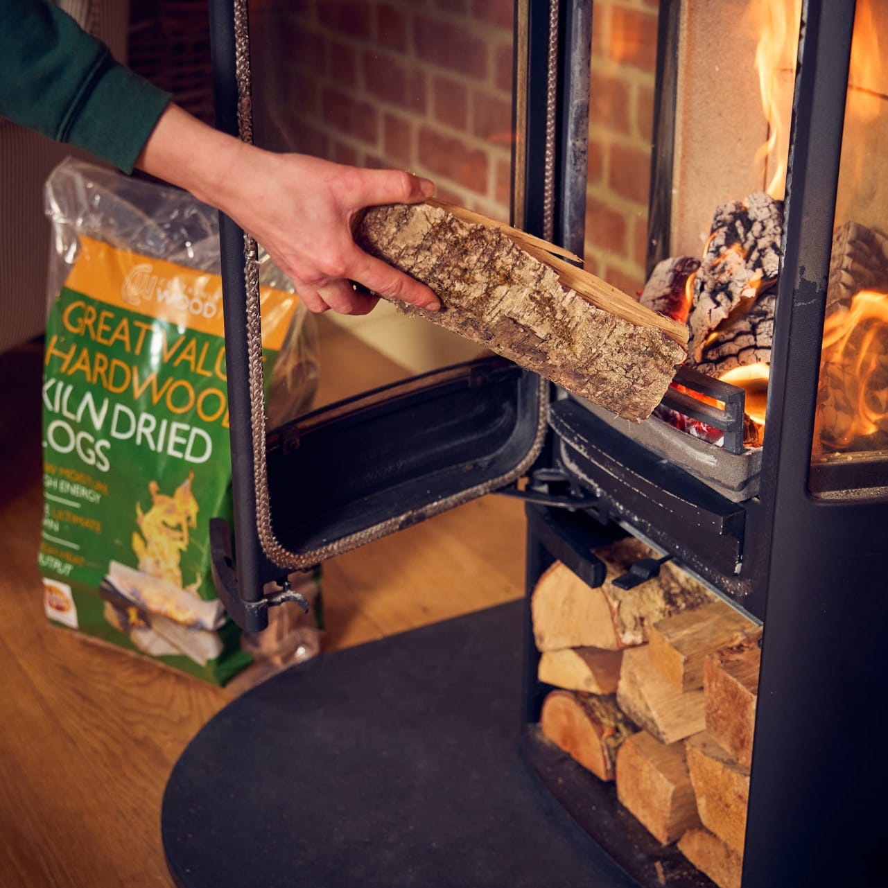 Person loading wood into a stove with a box of Great Value dried dog food nearby.