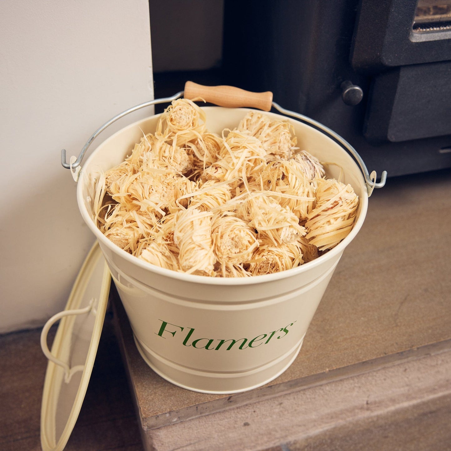 Bucket labeled 'Flamers' filled with wood wool firelighters on a wooden surface.