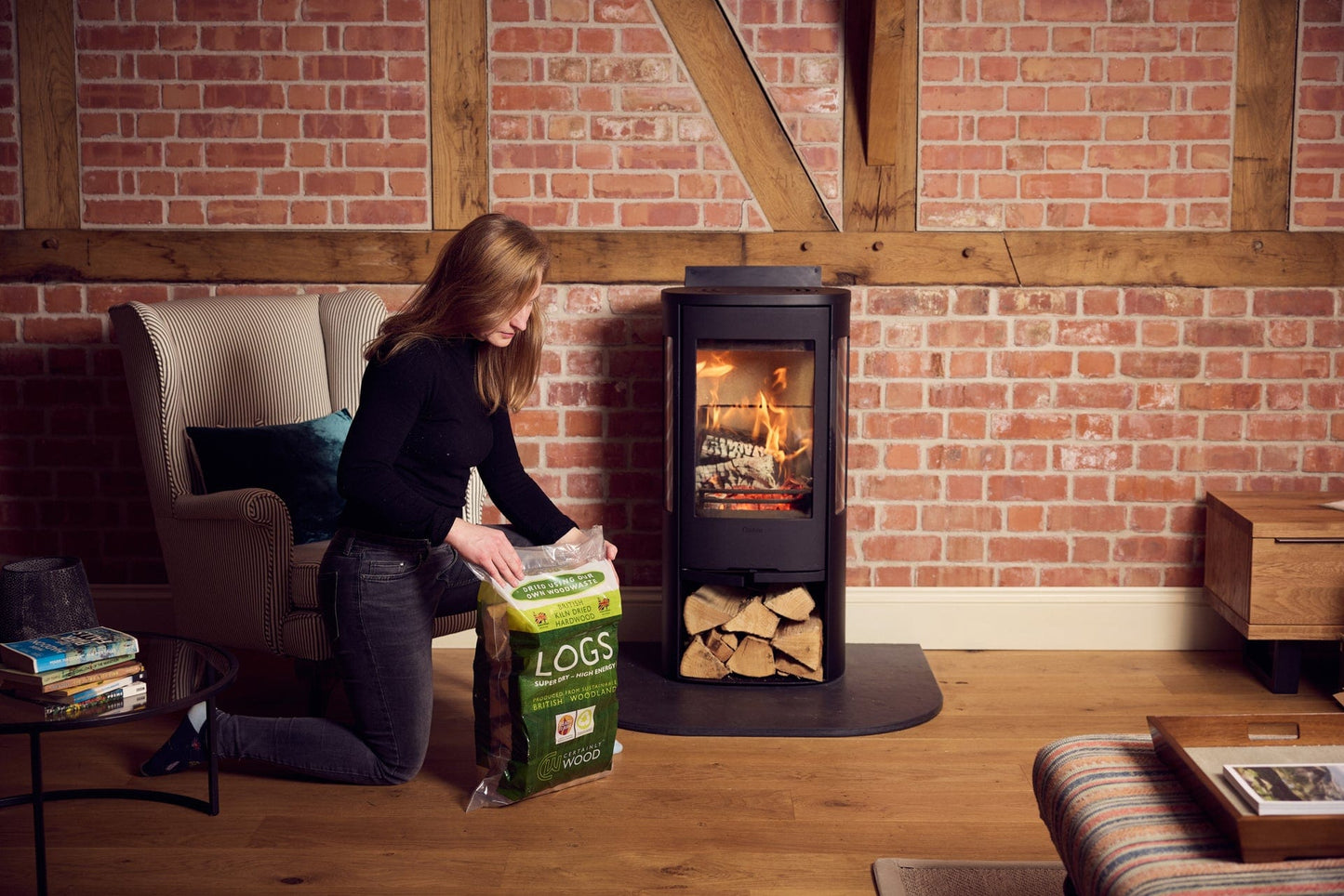 Woman unloading logs from a bag in front of a wood stove in a cozy living room.