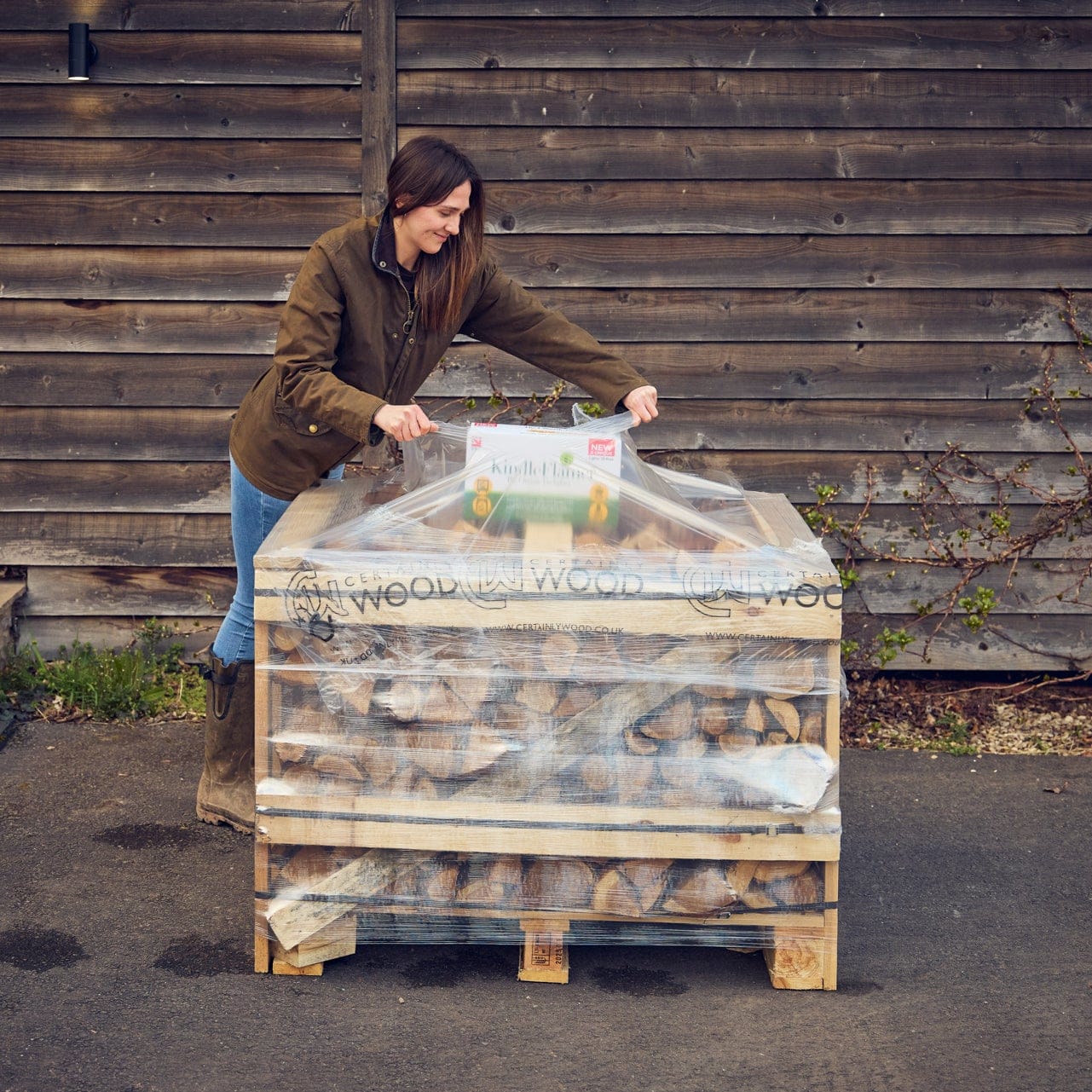 Person opening a stack of firewood with a weather proof cover against a wooden wall.